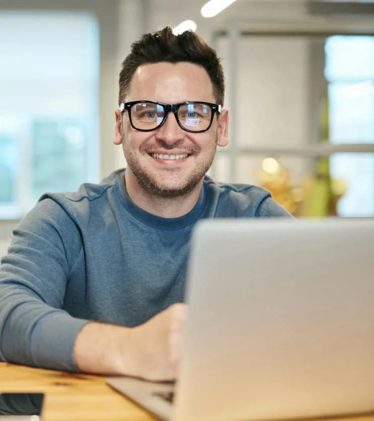 Ein lächelnder Mann mit Brille sitzt am Laptop