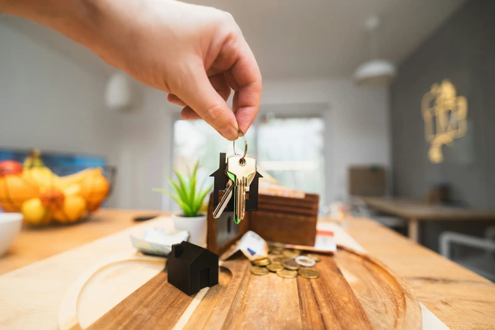 Eine Hand hält den Schlüssel mit Hausanhänger über den Holztisch einer hellen Küche